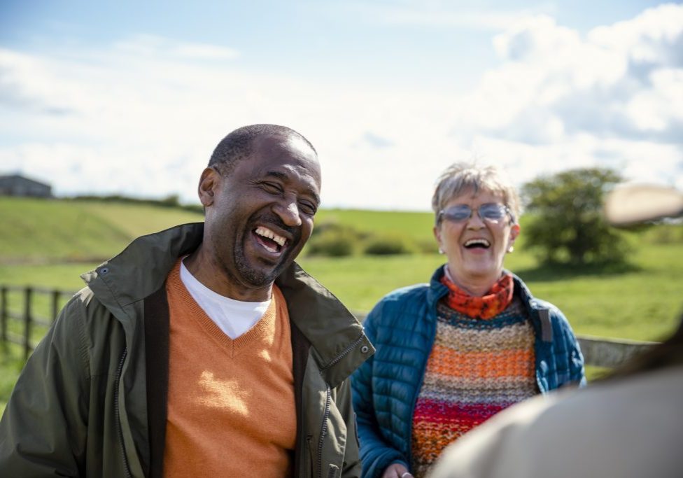 Senior friends standing in a field together while on staycation laughing and talking together. They are enjoying retirement together, being active in the North East of England.